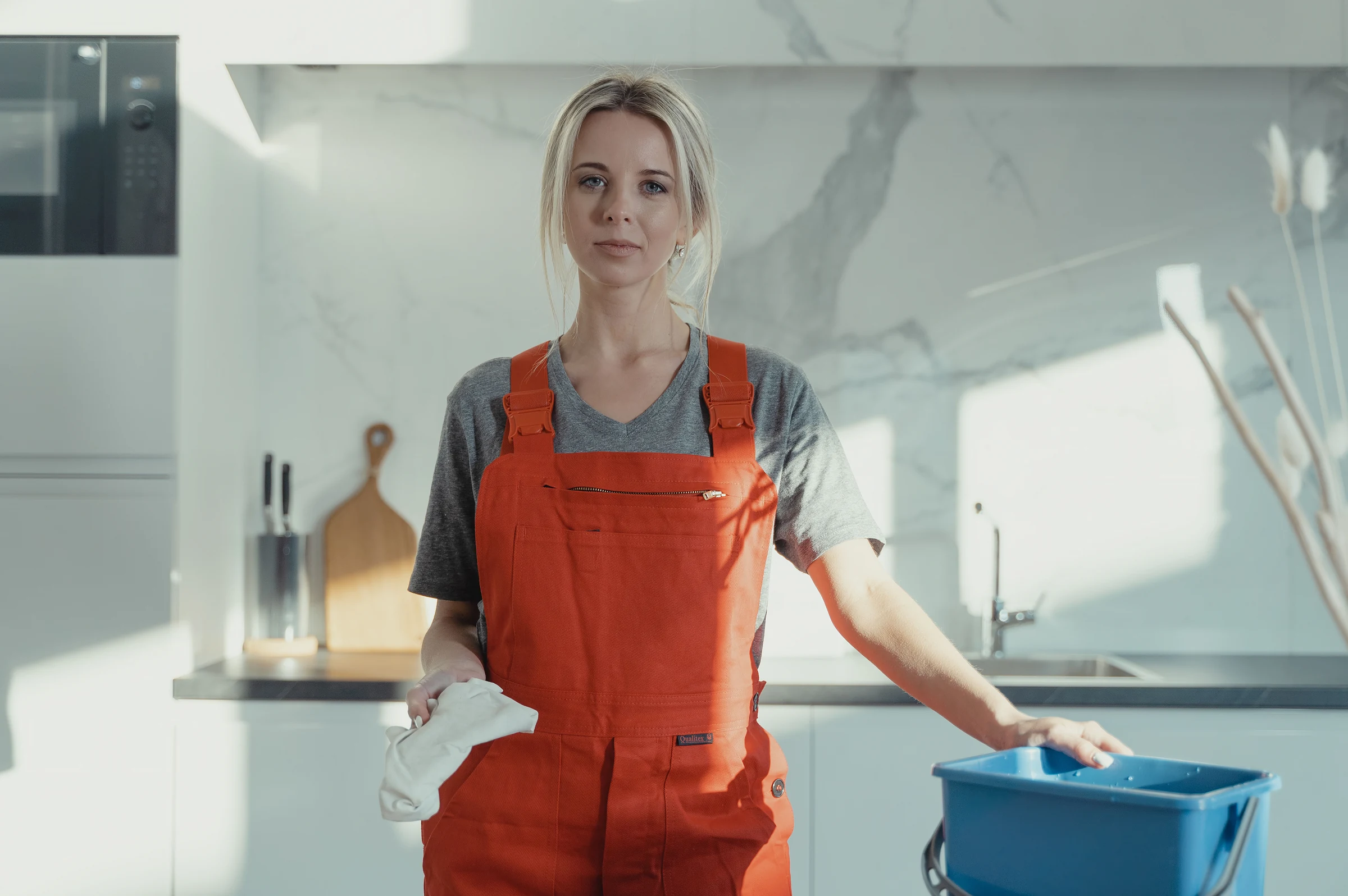 A cleaner in work overalls standing in a bright kitchen